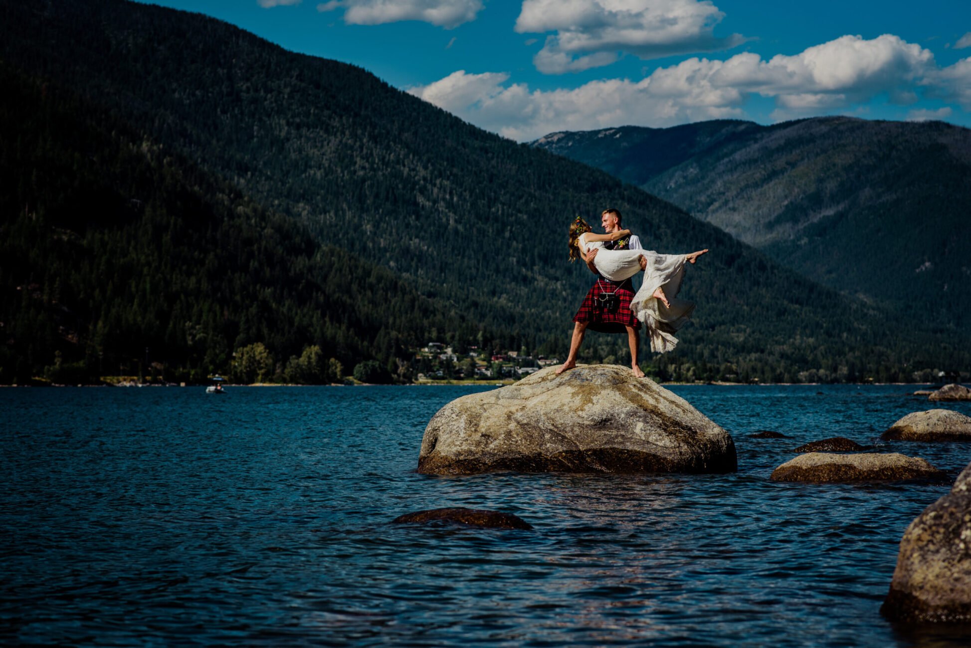 Groom holds his bride while standing on a rock at their lakeside wedding in Nelson BC